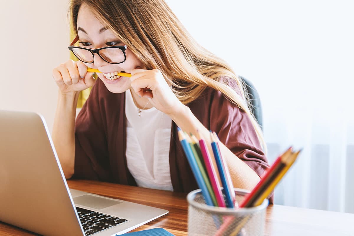 Someone with ADHD bites her pencil while working on her laptop.