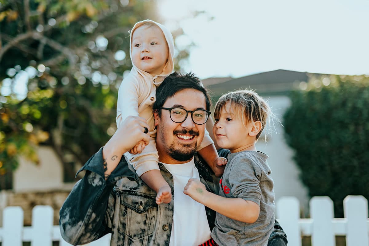 Father holding two young children outdoors and smiling