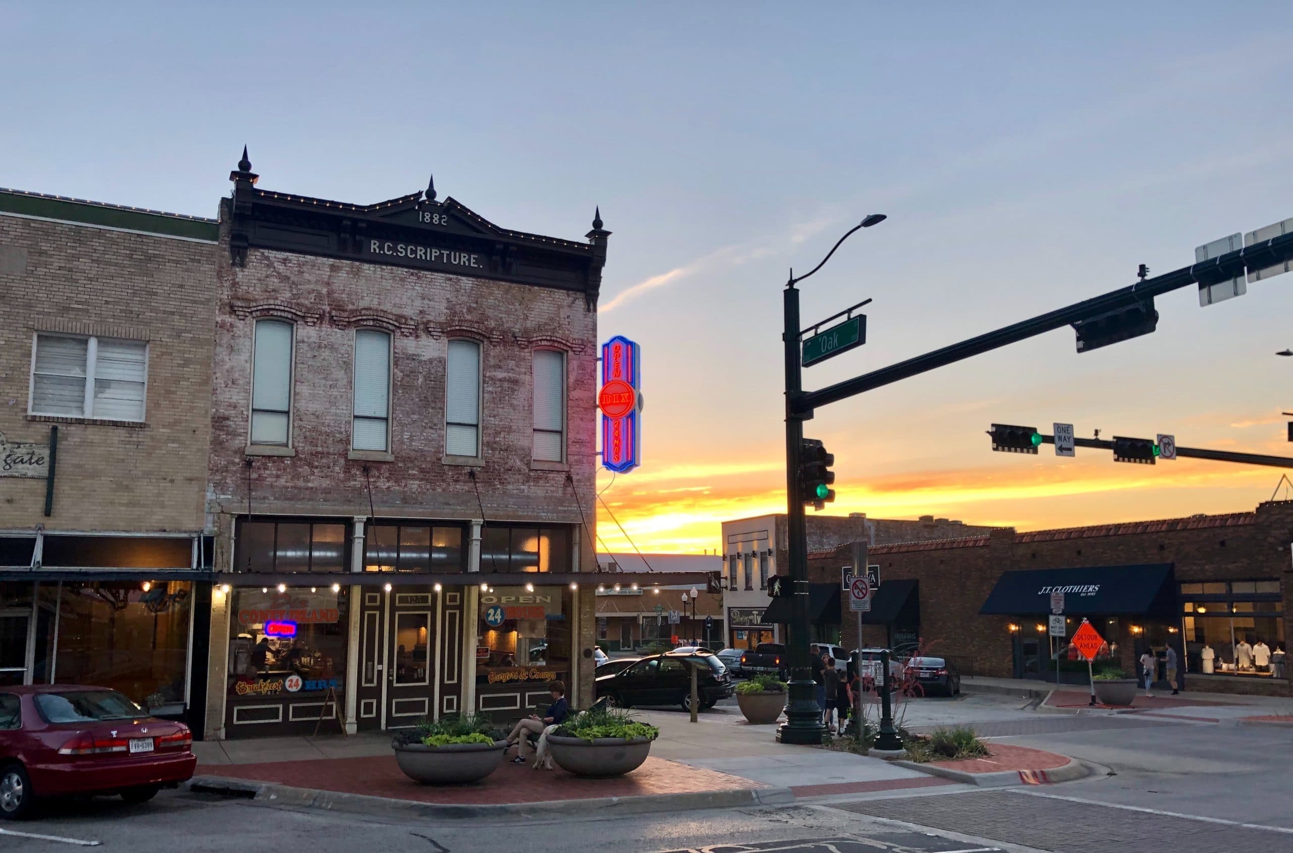 Monica Bourgeau Downtown street corner at sunset with historic storefronts and neon sign