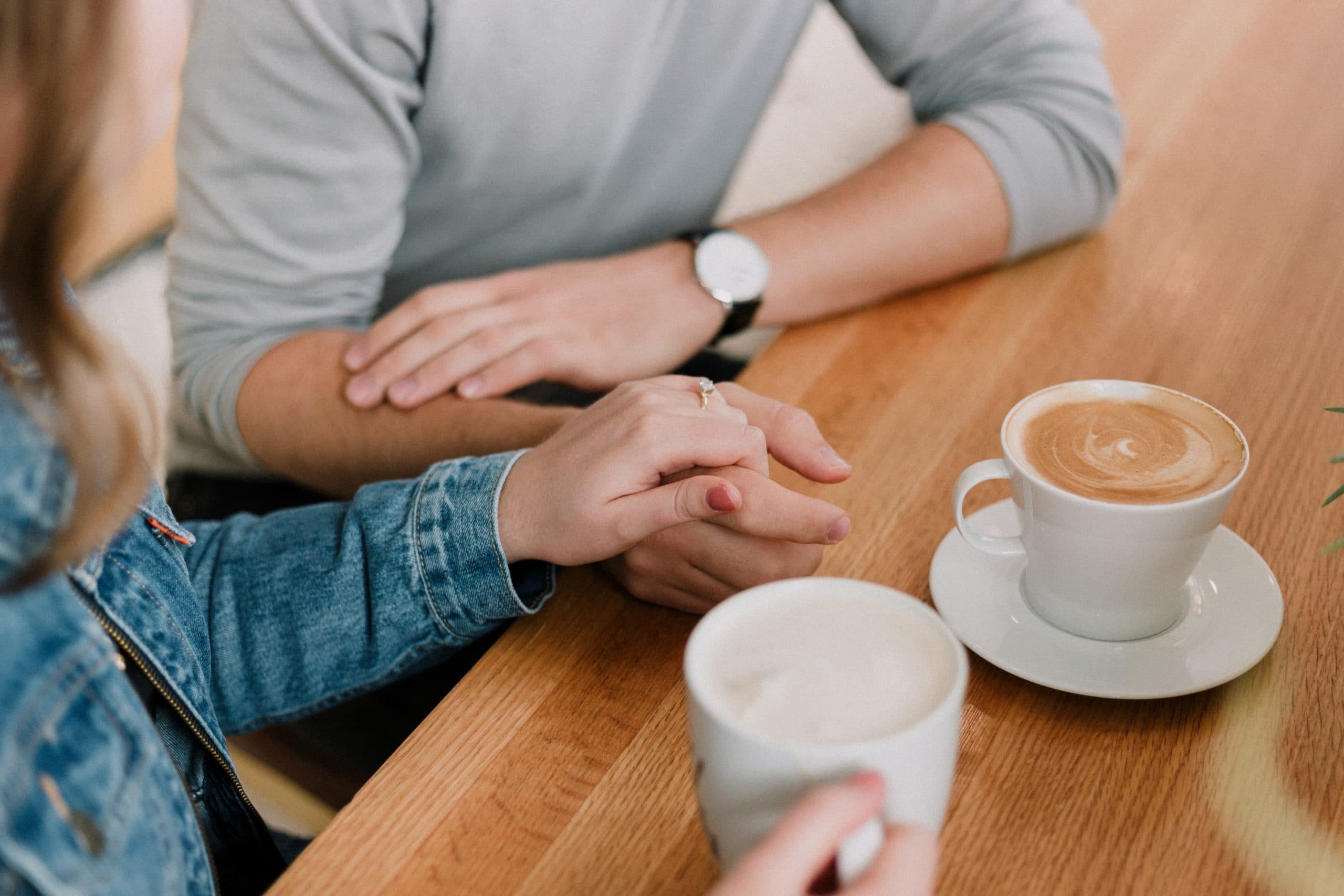 Couple holding hands across a table with coffee cups