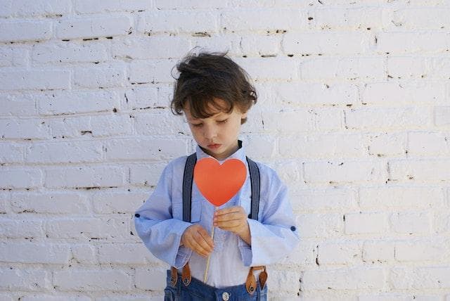 Little boy holding a paper heart looking down