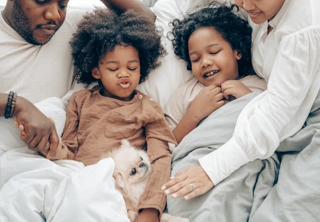 Family of four laying in a large bed covered with white sheets