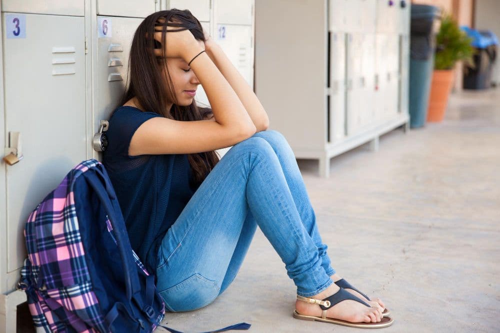 teenage girl sitting at lockers with her head in her hands
