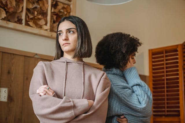 Two women standing angrily without looking at each other.