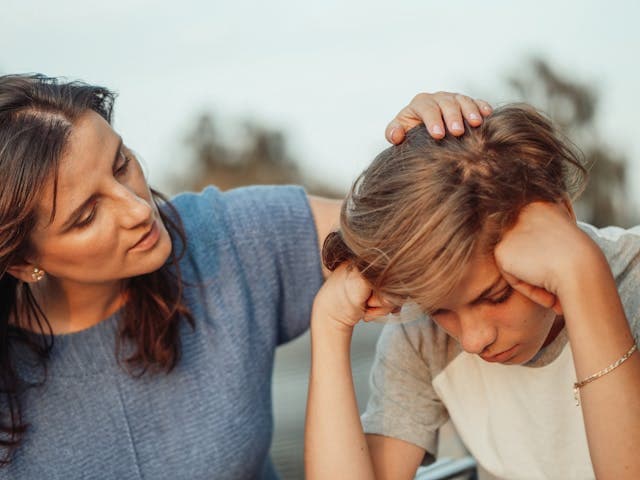 A woman gently touching a young teenager’s head.