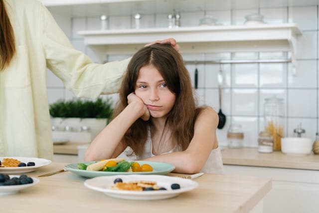 A teenage girl sitting at the kitchen table, sadly staring into the distance.