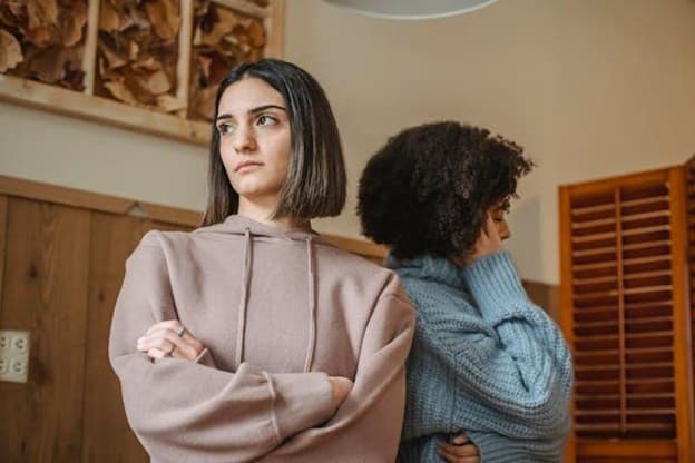 Two women standing angrily without looking at each other.